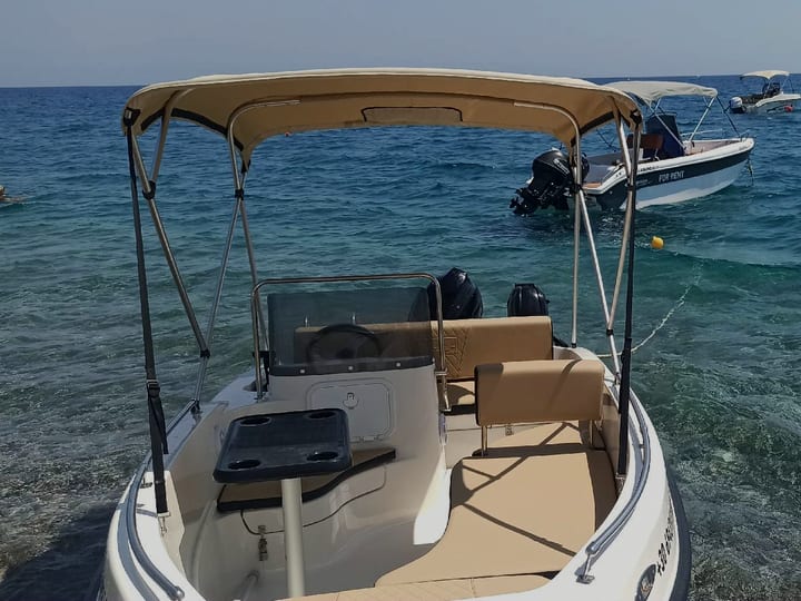 Die Nireus Optima im flachen Wasser: weißes Boot mit beigem Sonnensegel und beigen Sitzen, dahinter weitere Boote