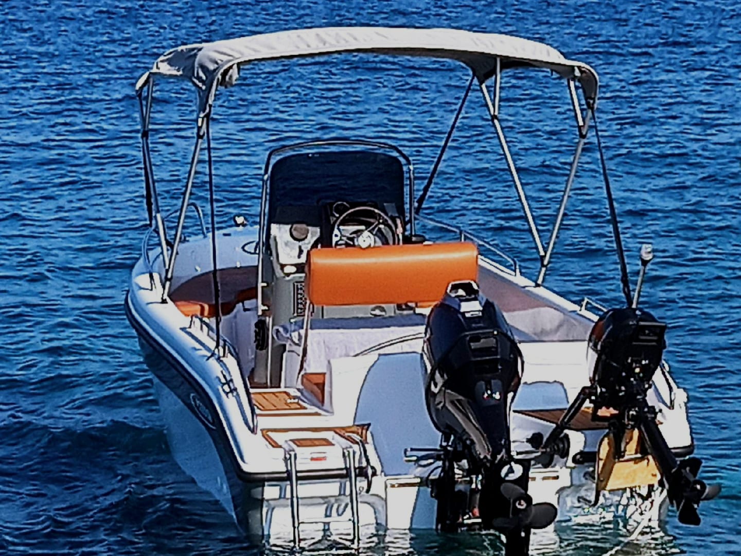 Die Poseidon Bluewater von hinten: graues Sonnensegel, orangefarbene gepolsterte Rückenlehne, zwei Außenborder, ruhiges blaues Meer