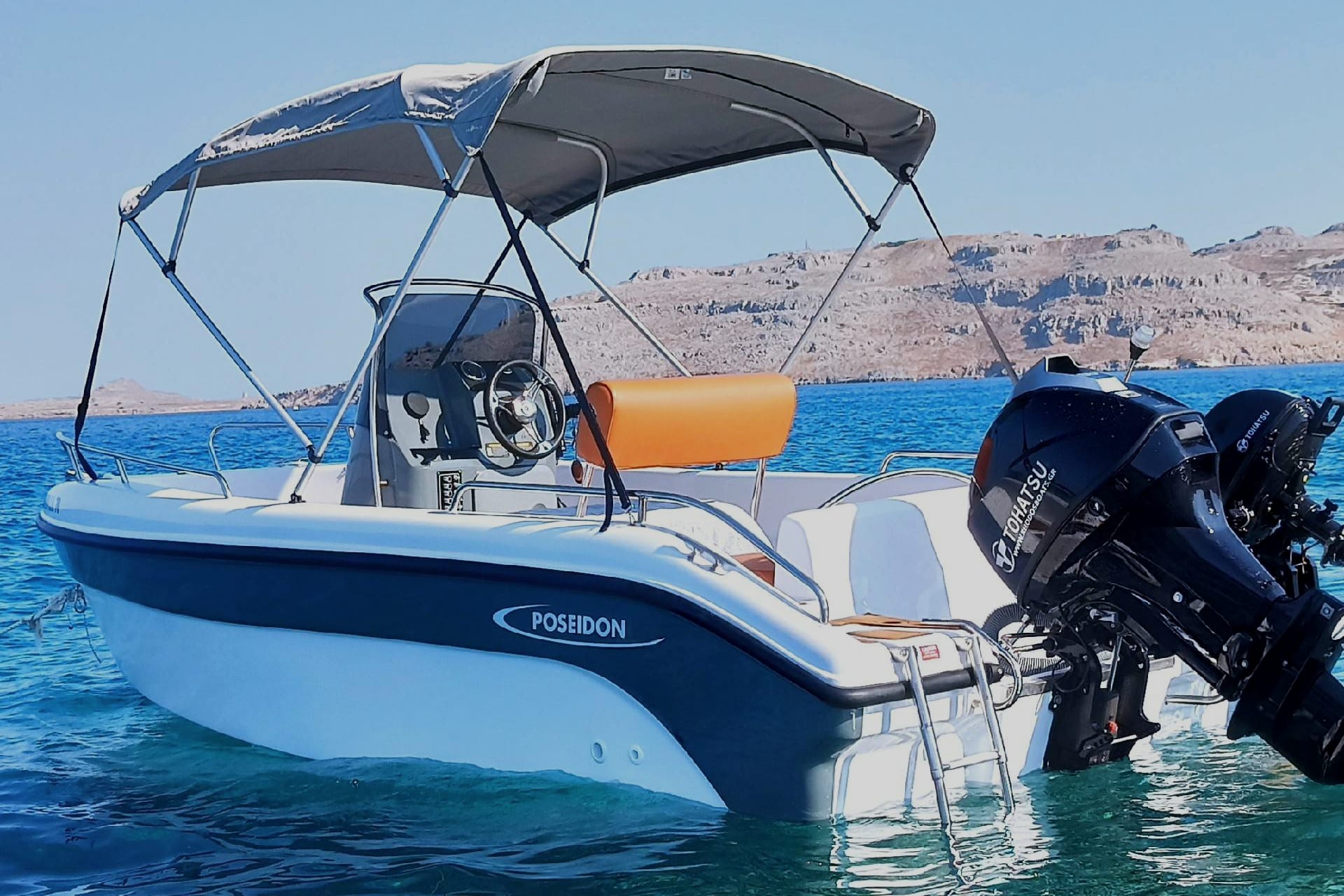Weißes Motorboot mit Sonnensegel und Badeleiter auf klarem blauem Wasser, dahinter eine felsige Küste