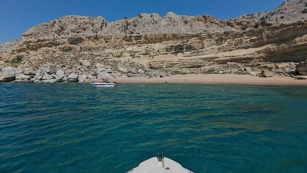 Blick vom Bug eines Boots auf eine helle Felsküste und einen Sandstrand